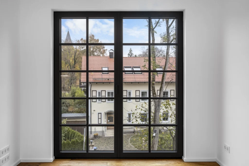 Large muntin window overlooking neighboring houses in an empty room of the rental apartment in Pöcking