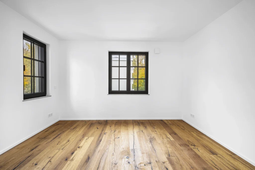 Empty room with two windows and hardwood floors in a rental apartment in Pöcking
