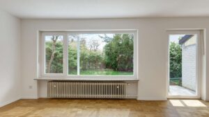 Empty living room with large window, patio door, and parquet flooring in the Putzbrunn house