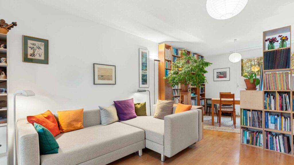 Open living room in Schwabing with a light-colored sofa, bookshelves, and a dining area in the background.