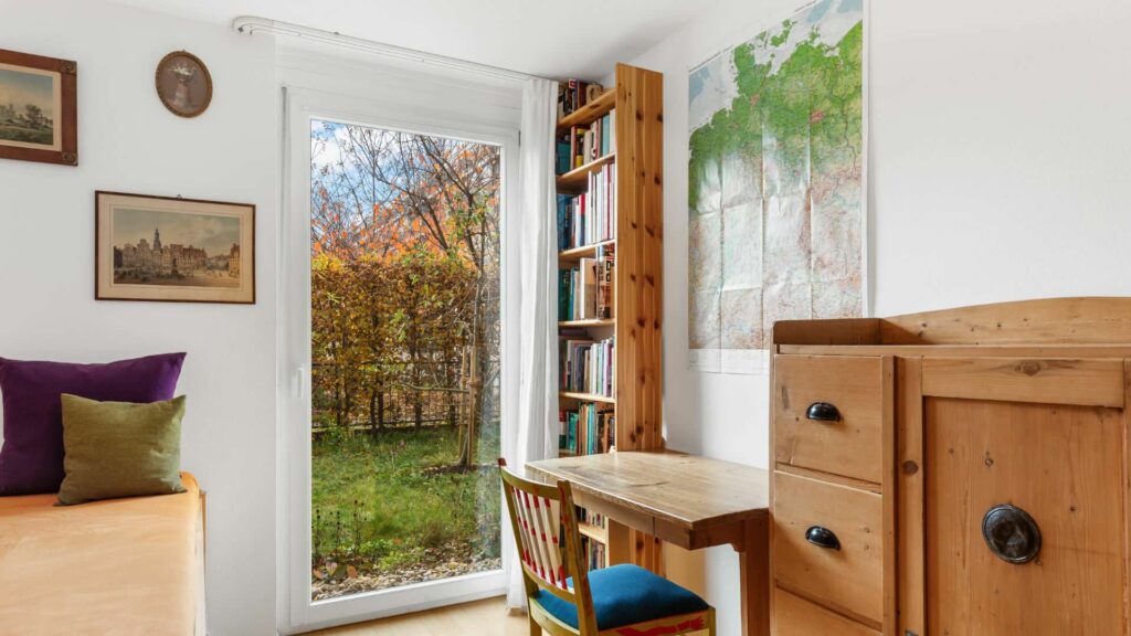 Room of the apartment in Munich-Schwabing with a bench, desk, and view of the garden
