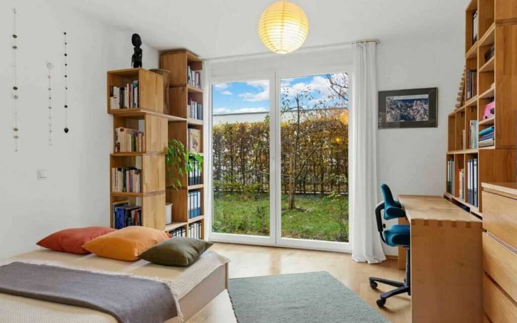 Children's room in Schwabing with a bed, bookshelf, desk, and view of the garden.