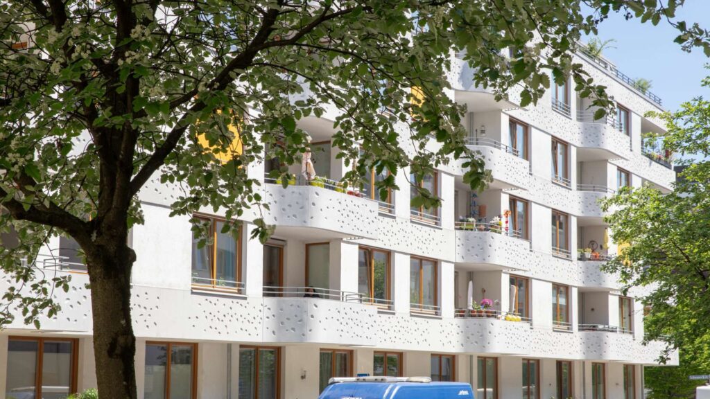 Moderne Hausfassade mit Balkonen hinter Baumkronen in Sendling