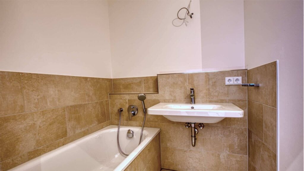 Schlichtes Badezimmer in Sendling mit Badewanne, Waschbecken und beigefarbenen Fliesen.