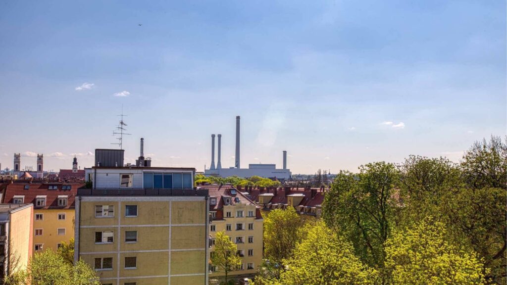 Blick vom Fenster über Dächer und Bäume mit Fernwärmetürmen im Hintergrund in München-Sendling