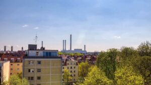 Blick vom Fenster über Dächer und Bäume mit Fernwärmetürmen im Hintergrund in München-Sendling