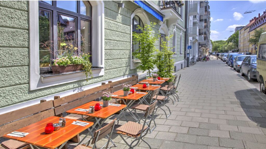 Straßencafé mit Tischen und Grün vor Altbaufassade in der Umgebung der Wohnung in Sendling