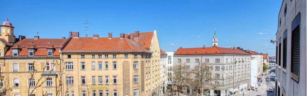 Blick über historische Altbaudächer und Fassaden im Münchner Stadtteil Sendling bei klarem Himmel.
