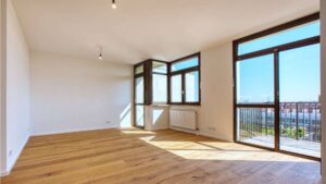 Leerer Wohnraum in Sendling mit großem Panoramafenster, Parkettboden und Blick auf die Nachbarschaft.