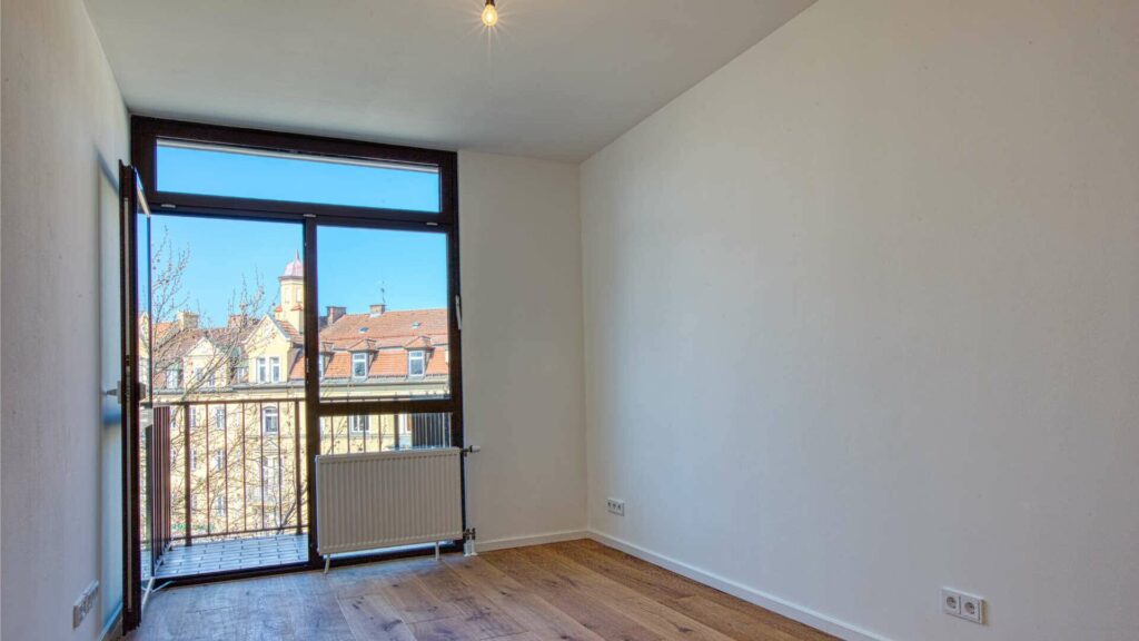 Leeres Zimmer mit raumhohem Fenster, Balkontür und hellem Parkettboden in der Wohnung in München-Sendling