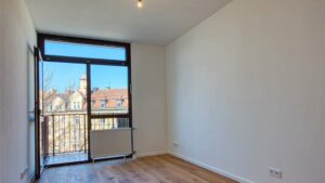 Leeres Zimmer mit raumhohem Fenster, Balkontür und hellem Parkettboden in der Wohnung in München-Sendling