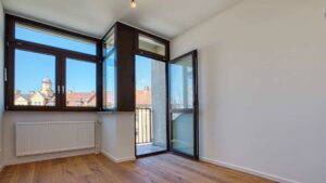 Leeres Zimmer mit Eckfenster, Balkonzugang und hellem Parkettboden in der Wohnung in München-Sendling