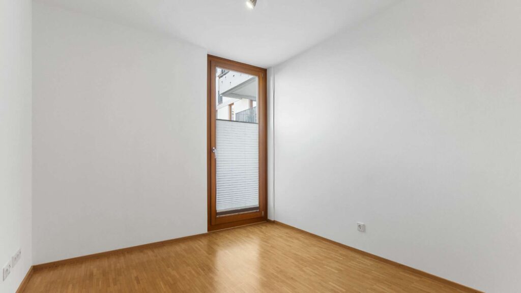 Leeres, helles Zimmer mit Parkettboden und Balkonzugang in einer Wohnung in Sendling