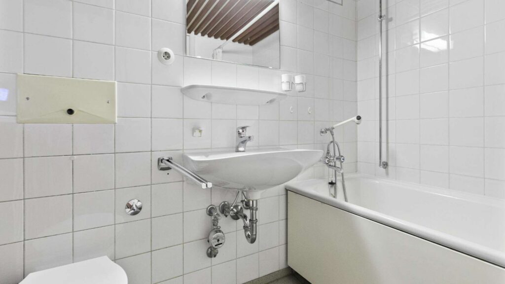 Badezimmer der Wohnung in München-Solln mit weißen Fliesen, Waschbecken und Badewanne