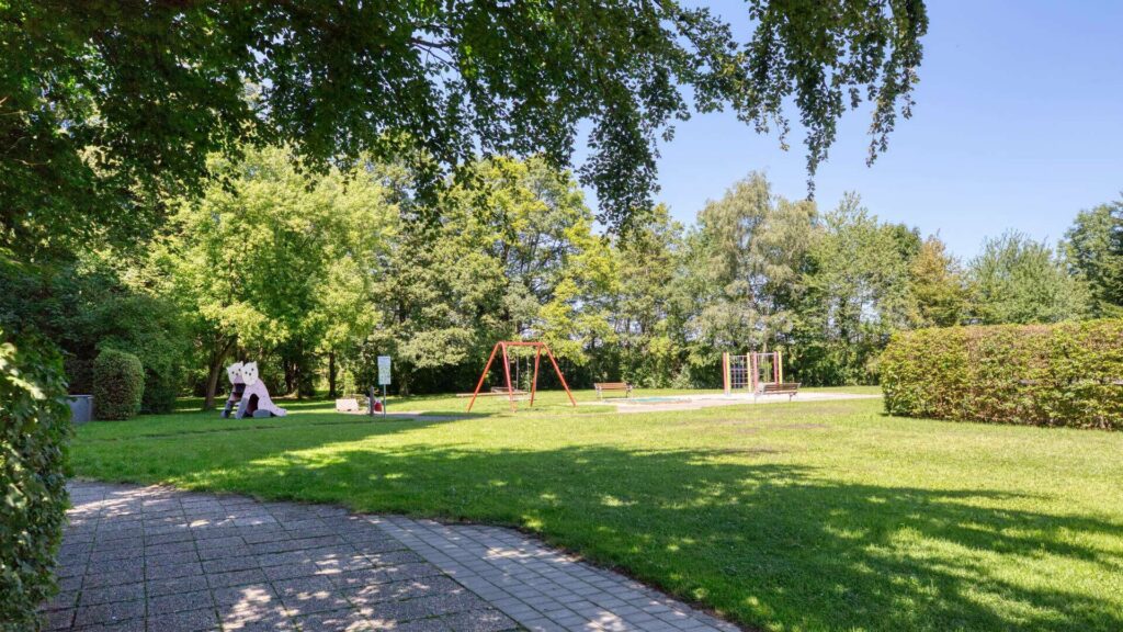 Grünanlage der Wohnanlage in München-Solln mit Rasenfläche, Spielplatz und gepflasterten Wegen