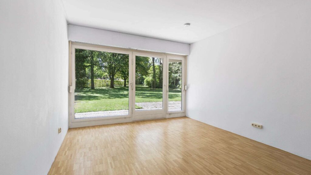 Leeres Schlafzimmer in Solln mit großer Fensterfront, Parkettboden und Blick ins Grüne.