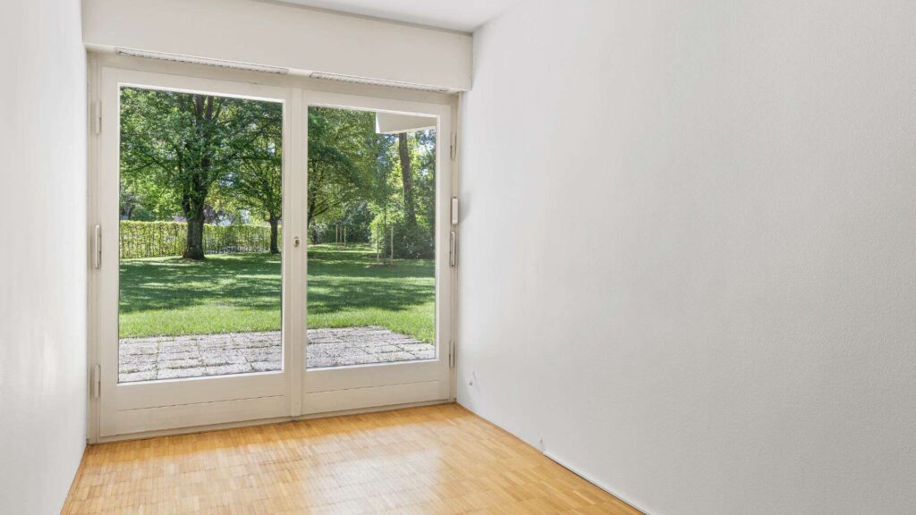 Leeres Zimmer der Wohnung in München-Solln mit Parkettboden und Terrassentür in den Garten