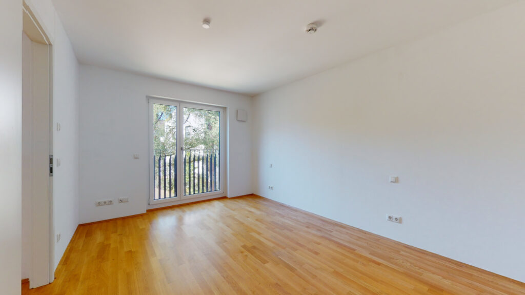 Empty bedroom with balcony door and parquet flooring in a newly built apartment in Munich-Berg am Laim
