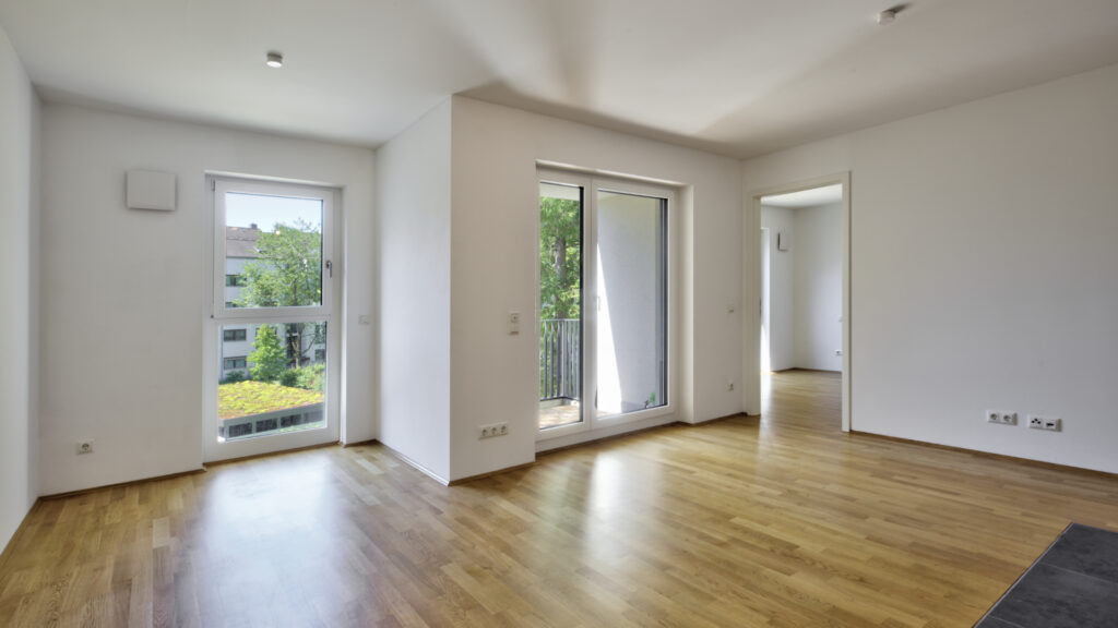 Empty living room with balcony access and parquet flooring in a newly built apartment in Munich-Berg am Laim