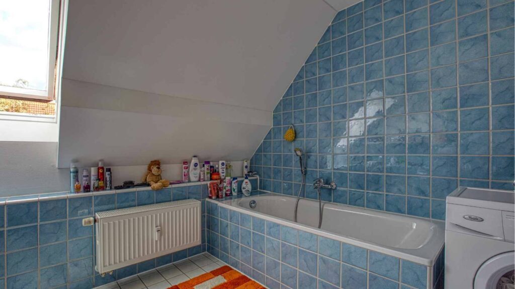 Existing bathroom with blue tiles, bathtub, and washing machine in the attic in Munich-Trudering