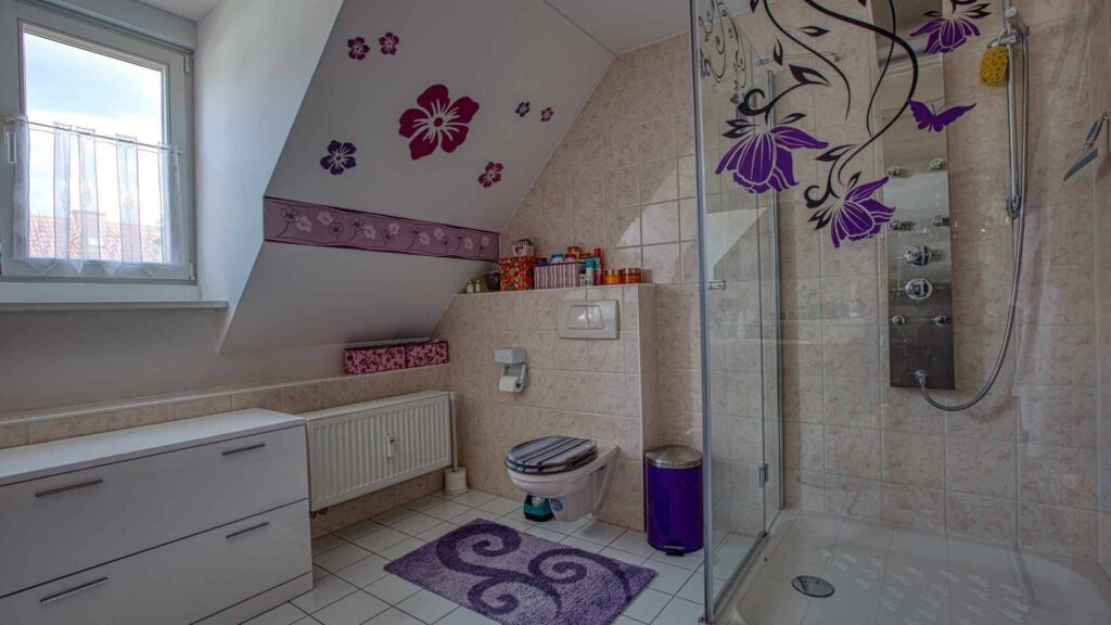 Small bathroom with floral tile motifs, shower, and toilet in the attic in Munich-Trudering