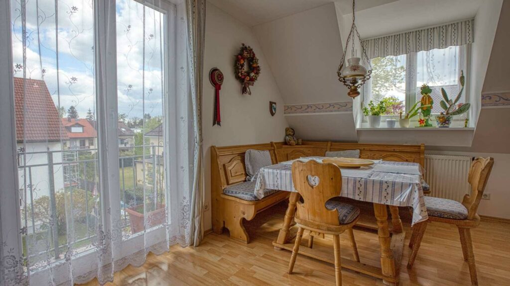 Dining area under the sloped ceiling in Trudering with a rustic wooden table and balcony access.