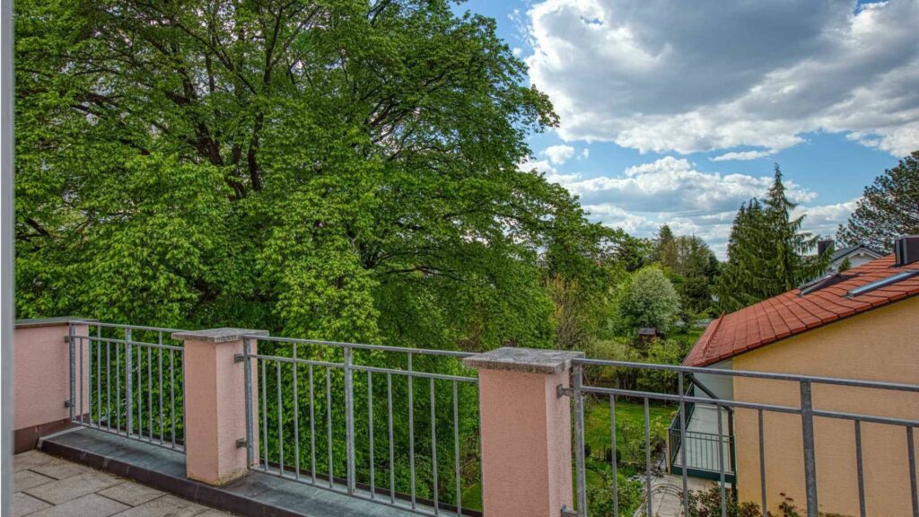 Roof terrace with railing and views of trees and neighboring houses of the apartment in Munich-Trudering