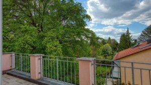 Roof terrace with railing and views of trees and neighboring houses of the apartment in Munich-Trudering