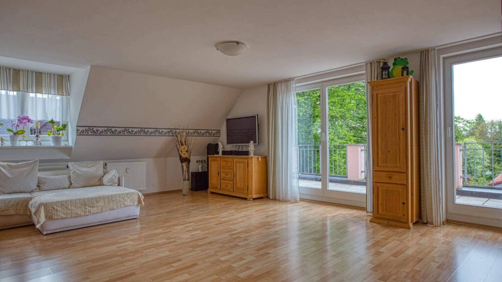 Bright living room under the sloped roof in Trudering with a white sofa and parquet floor.