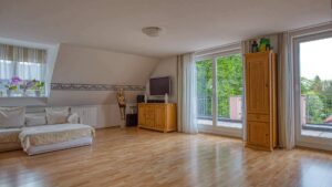 Bright living room under the sloped roof in Trudering with a white sofa and parquet floor.