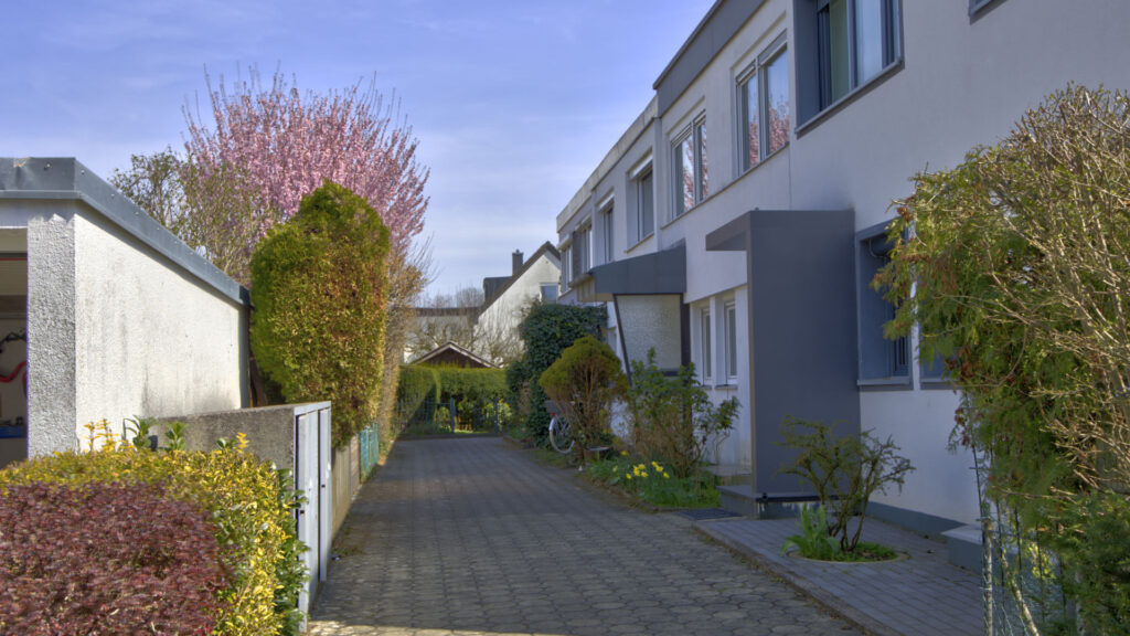Paved access road between terraced houses with a flowering tree in Unterhaching near Munich