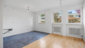 Leeres Zimmer mit Parkett- und Teppichboden-Kombination und zwei Fenstern in Unterhaching