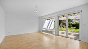 Leerer Wohnraum mit schräger Decke, großer Fensterfront und hellem Holzboden in Reihenendhaus Unterhaching