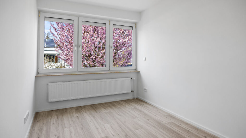 Empty room with window and view of flowering tree in a row house for rent in Unterhaching