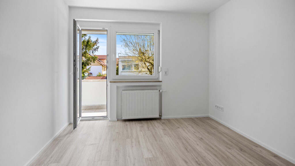Empty room with balcony door and view of the greenery in a row house for rent in Unterhaching near Munich