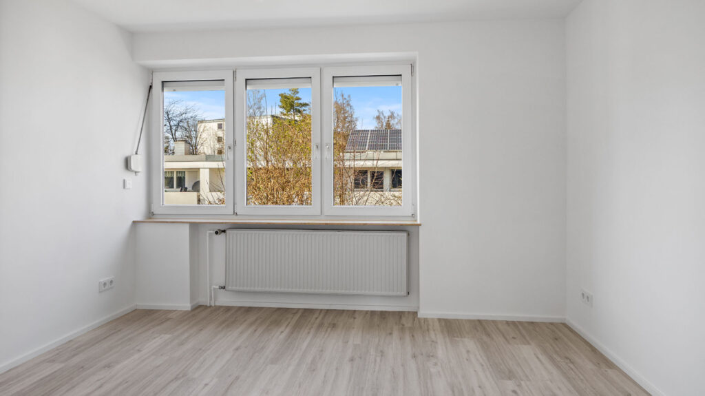 Empty, bright room with wooden floors, white walls and a window to the end of a row of houses in Unterhaching near Munich