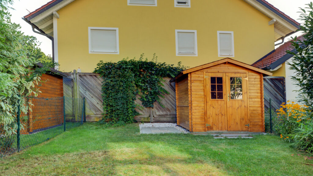 A wooden garden shed in front of a yellow house in Germering