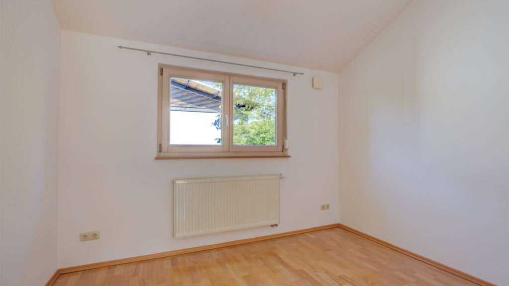 Small empty room with a window and radiator in an apartment building in Germering