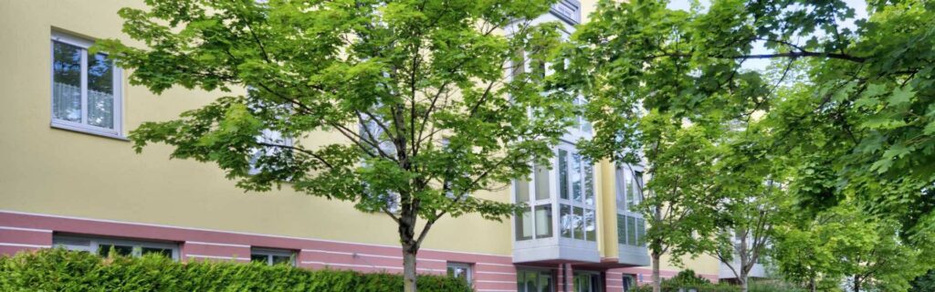 Fassade des Wohngebäudes in Berg am Laim, teilweise verdeckt von grünen Baumkronen