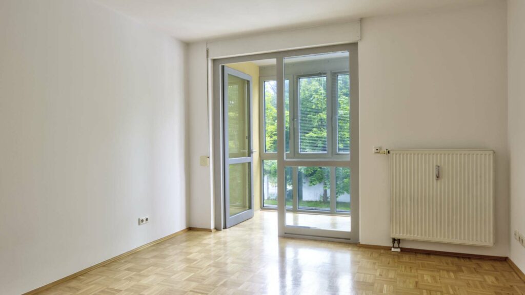 Leeres Zimmer der Wohnung in Berg am Laim mit Balkontür, Heizkörper und Parkettboden