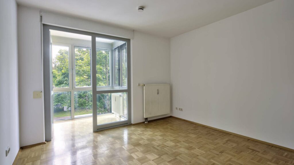 Leeres Zimmer der Wohnung in Berg am Laim mit Terrassentür, Parkettboden und Grünblick