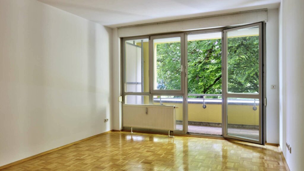Leeres Wohnzimmer der Wohnung in Berg am Laim mit Parkettboden, Balkontür und Grünblick
