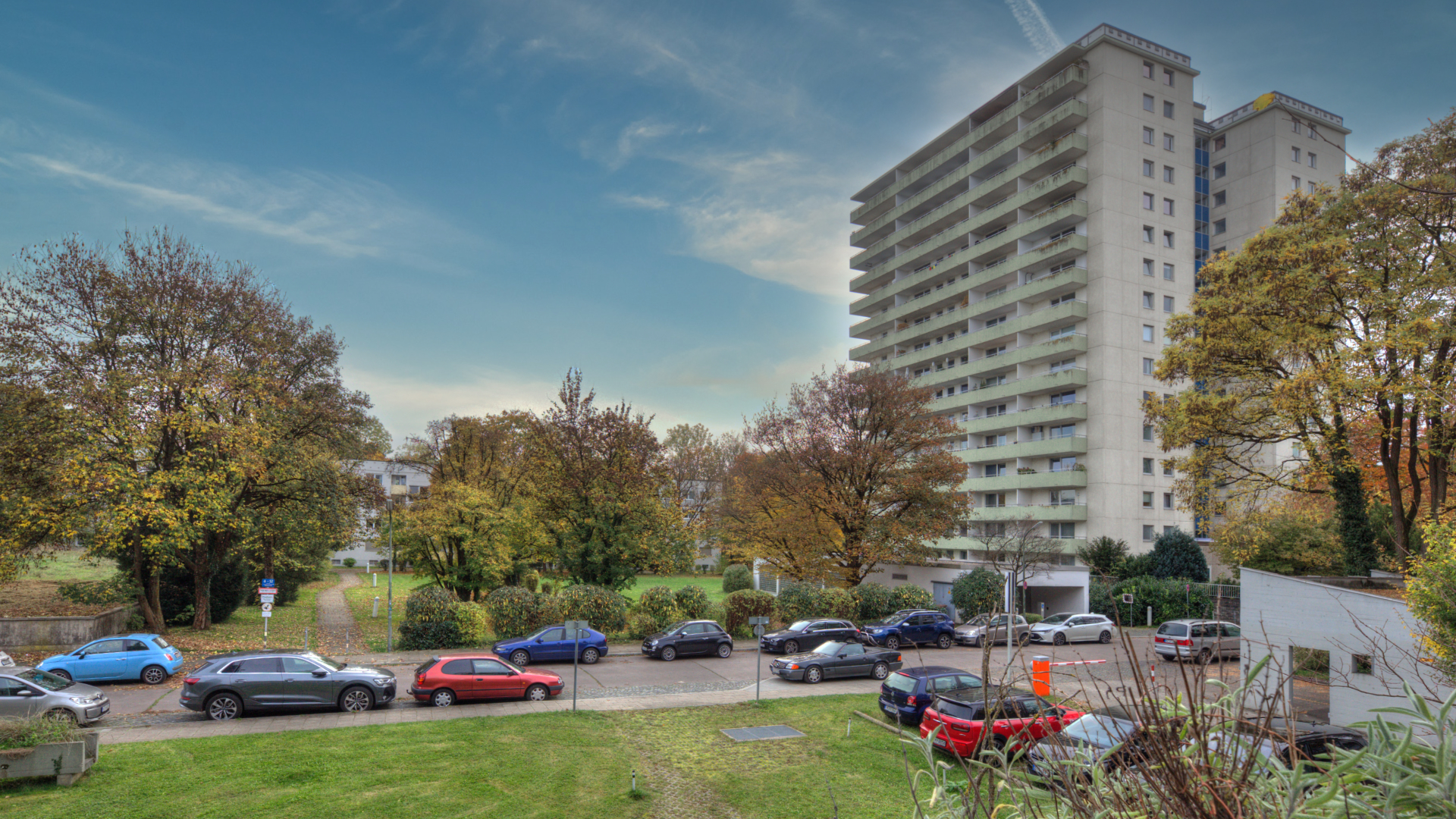 View across a green space with parked cars toward a high-rise residential building in Munich-Bogenhausen