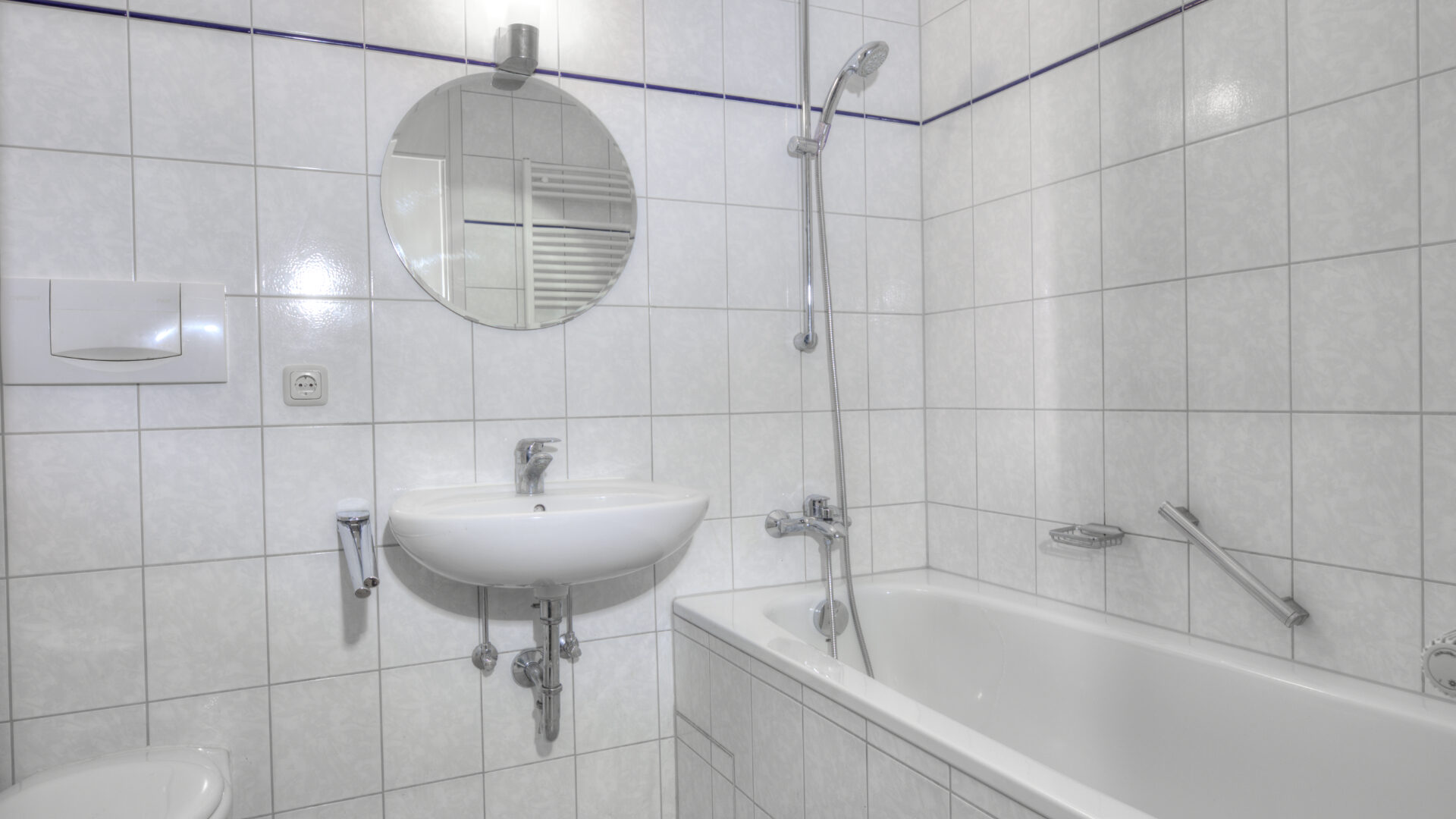 Bathroom with white tiling, round mirror, sink, and bathtub in an apartment in Munich-Bogenhausen