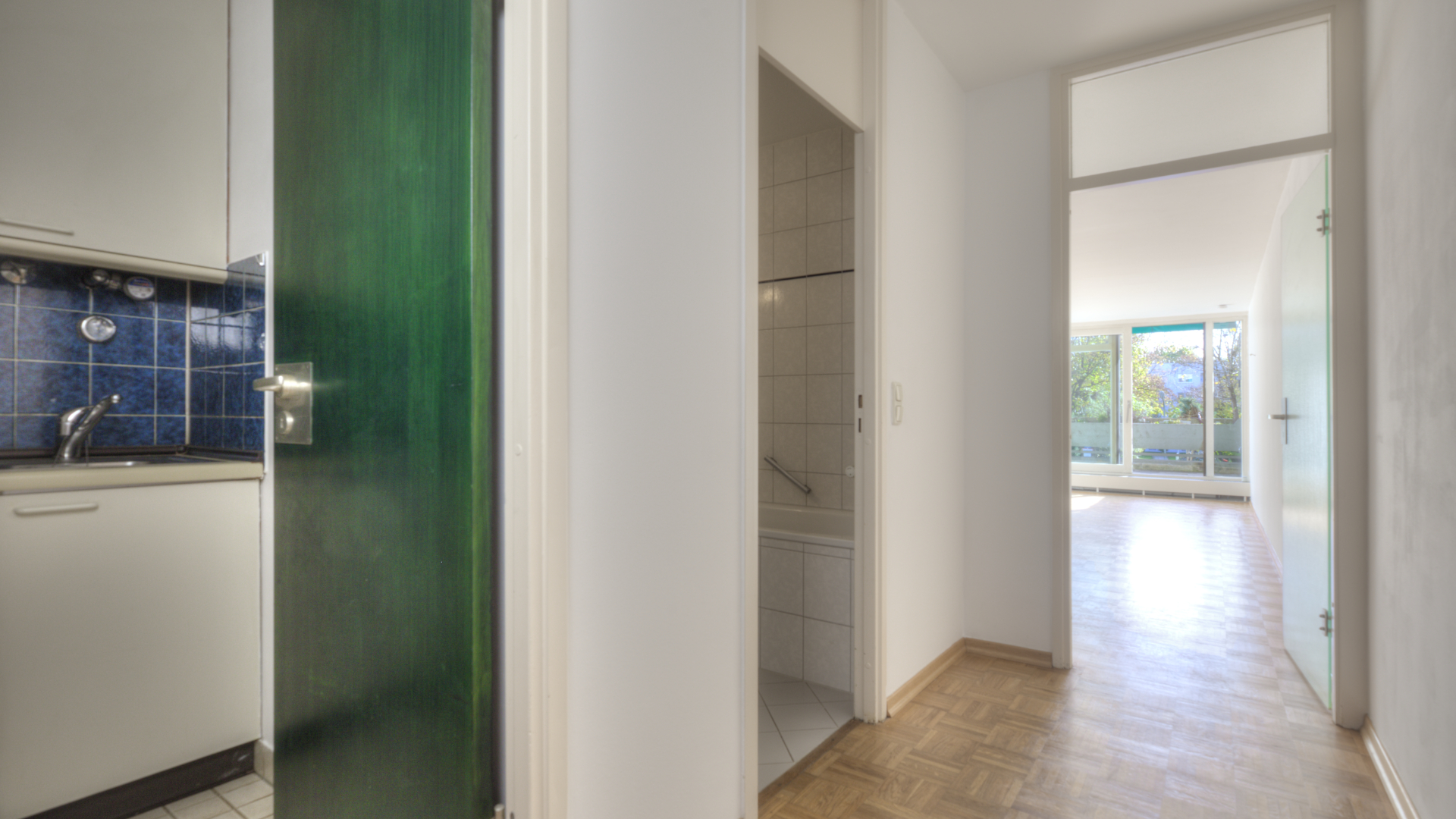 Entrance area with a green kitchen door and view through the hallway to the terrace and greenery in an apartment in Munich-Bogenhausen