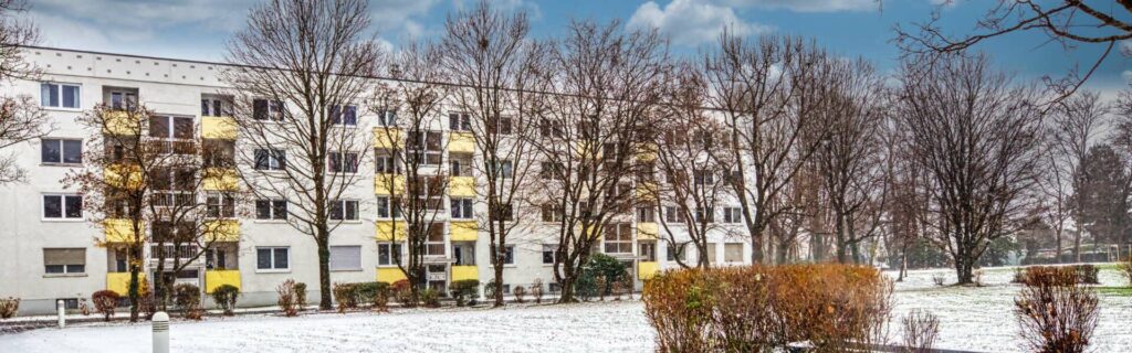 Panoramic view of the yellow-and-white facade of a block of flats with balconies in the snow in Munich-Bogenhausen