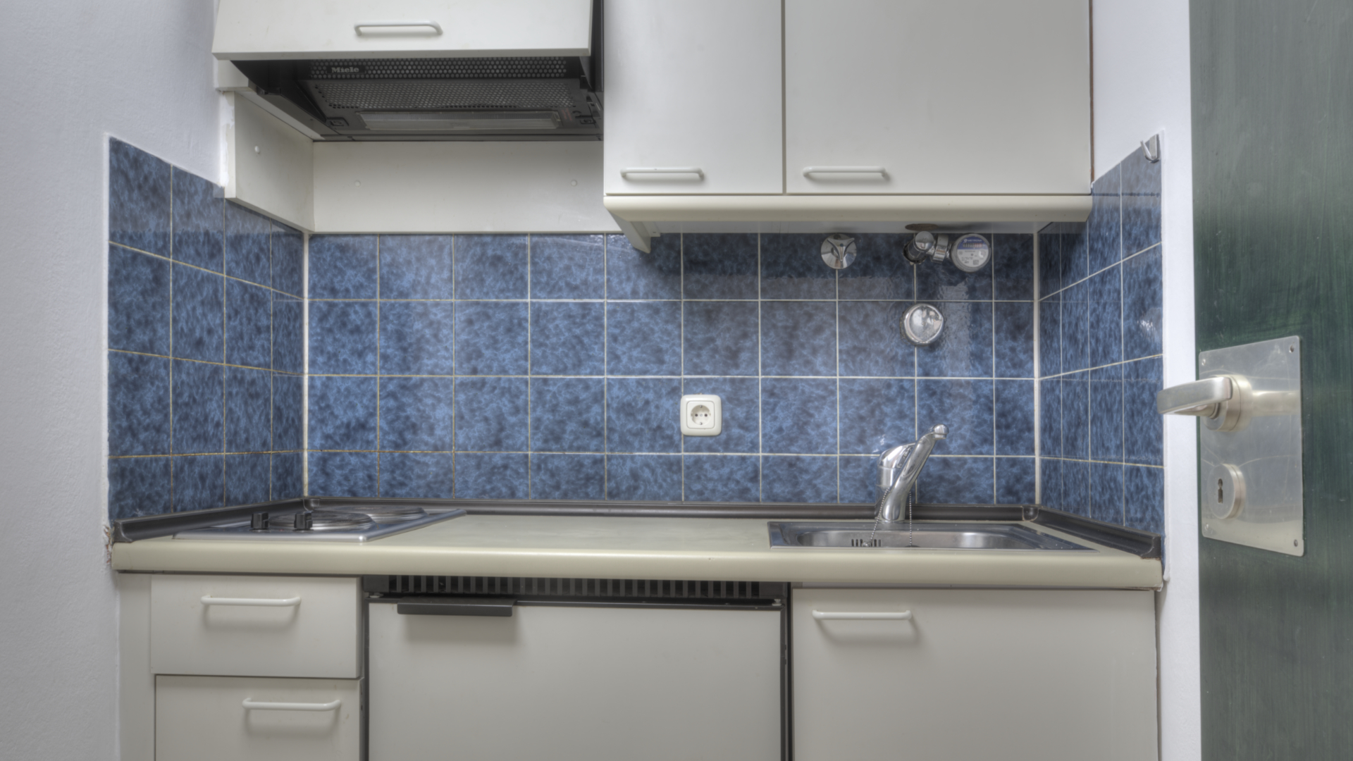 Small unrenovated kitchen with blue tiles and white cabinets in an apartment in Munich-Bogenhausen