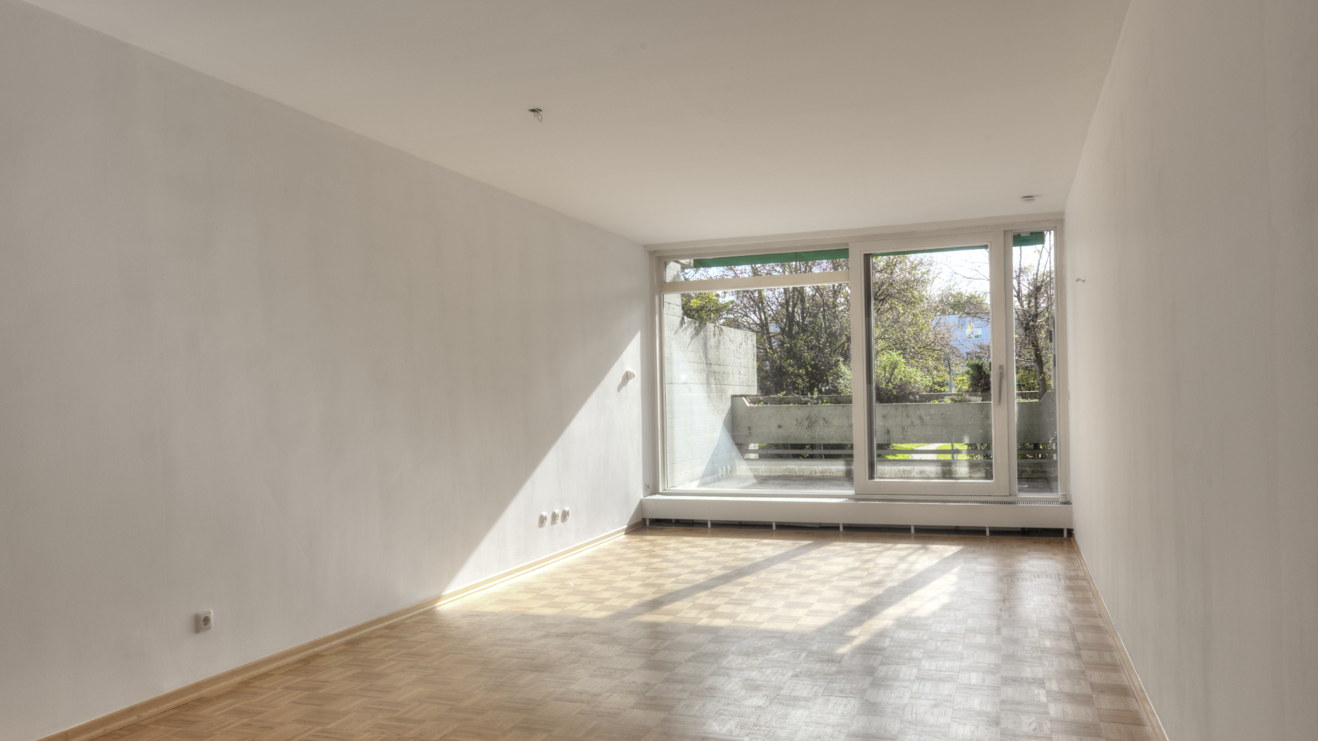 Unfurnished room with parquet flooring and large floor-to-ceiling windows leading to the terrace in an apartment in Munich-Bogenhausen