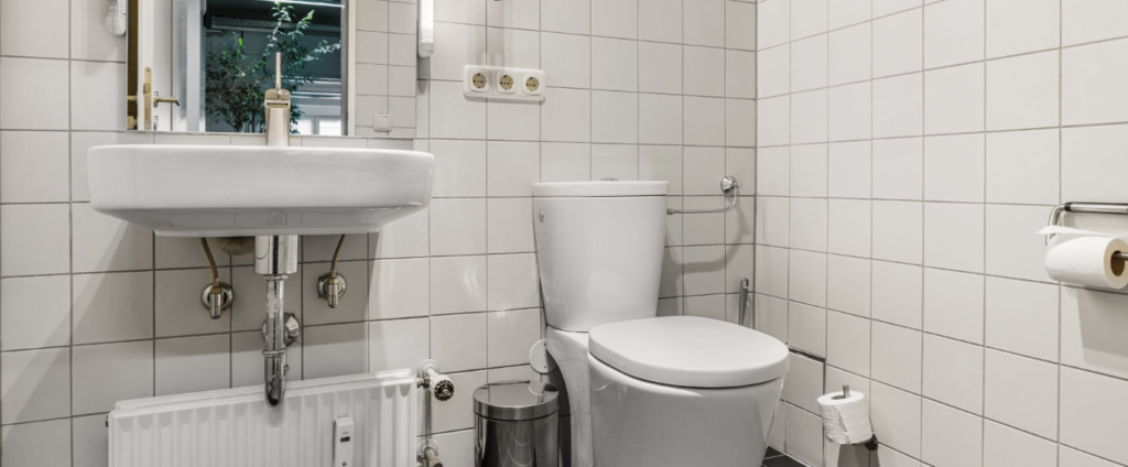 Older bathroom with white tiles, sink, and toilet before renovation