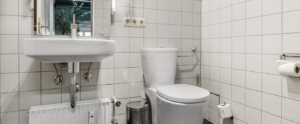 Older bathroom with white tiles, sink, and toilet before renovation